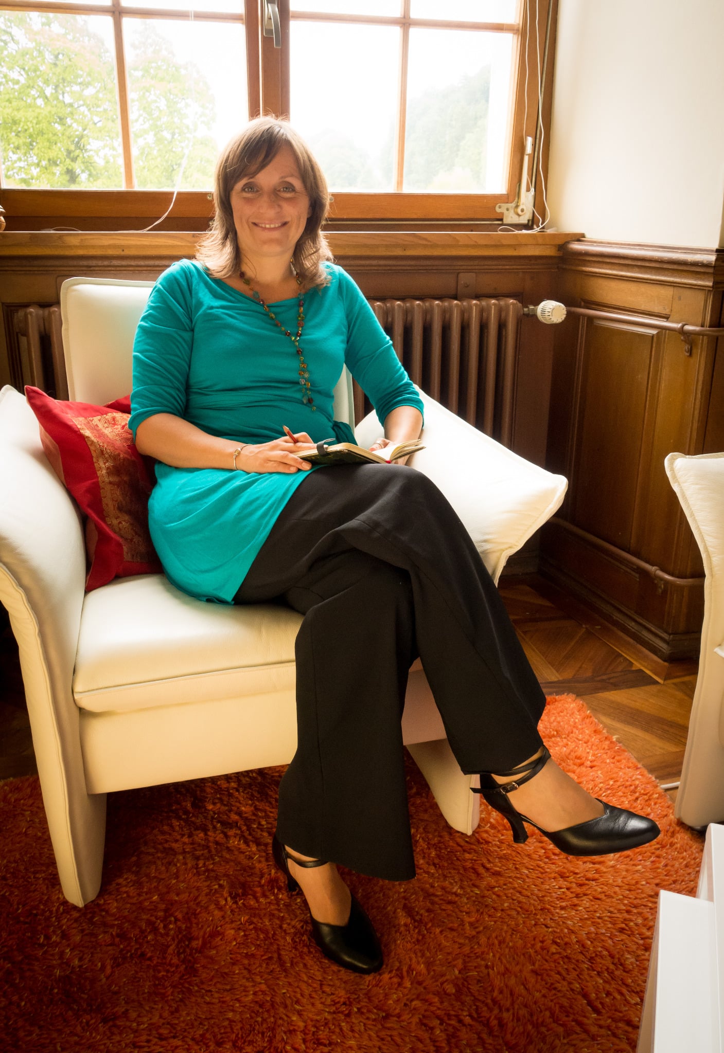Christine Dürschner mit Notizbuch im weissen Sessel